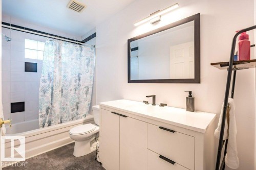White vanity with black hardware, white countertop, and rectangular mirror - 4705 43 Street, Beaumont, AB 