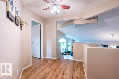 Wood-finish flooring throughout, ceiling fan with integrated lighting, architectural ceiling beams, and a half-wall overlooking a lower level - 4705 43 Street, Beaumont, AB 