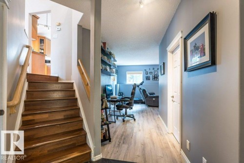 Wood-finish flooring, staircase with wood treads and handrail, track lighting, white paneled doors, and a built-in shelving unit - 4705 43 Street, Beaumont, AB 
