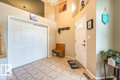 Foyer with tiled flooring, white paneled entry door with an arched window, and a white paneled bi-fold closet - 4705 43 Street, Beaumont, AB 