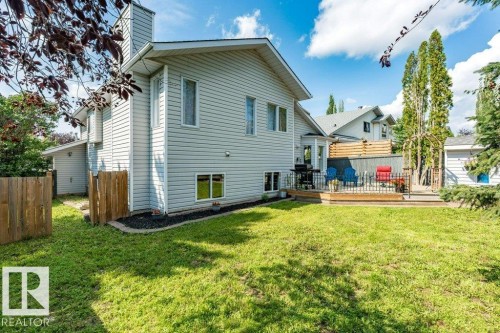 Expansive backyard featuring a manicured lawn, a raised wooden deck with metal railing, and a privacy fence - 4705 43 Street, Beaumont, AB 