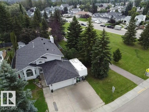 Gabled roof with dark shingles, two-car attached garage, paved driveway, mature conifer landscaping, and a bay window - 4705 43 Street, Beaumont, AB 