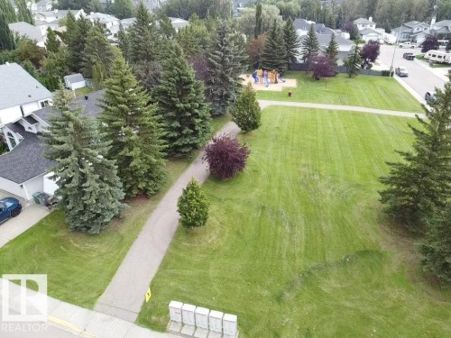 Expansive green space featuring a paved pathway, mature trees, and a playground structure - 4705 43 Street, Beaumont, AB 
