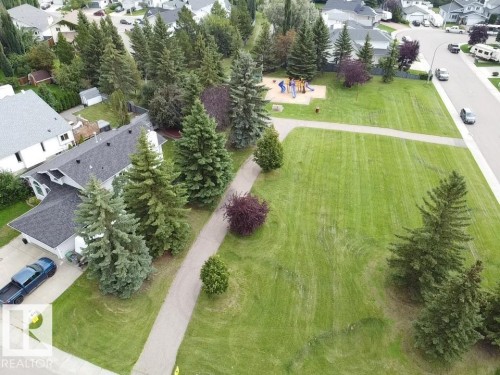 Expansive green space featuring a playground structure, paved walking paths, mature trees, and street access - 4705 43 Street, Beaumont, AB 