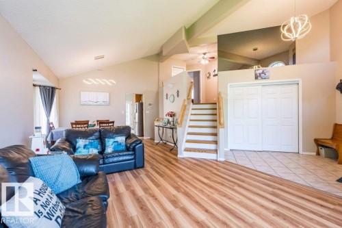 Vaulted ceilings, wood-finish flooring, staircase with wood handrail, dining area with modern pendant lighting, and a kitchen visible in the background - 4705 43 Street, Beaumont, AB 