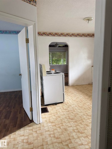 Arched doorway leading to a room with a window, checkerboard-patterned flooring, and a flush-mount ceiling light fixture - 5518 51 Street, Vegreville, AB - Indoor Photo Showing Other Room