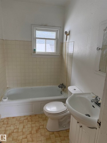 Bathroom featuring a built-in bathtub, a window, a wall-mounted shower fixture, a toilet, and a vanity with an integrated sink - 5518 51 Street, Vegreville, AB - Indoor Photo Showing Bathroom