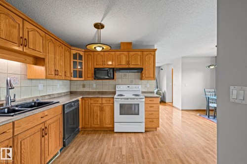 Kitchen featuring wood cabinetry, tiled backsplash, and wood-finish flooring - 17908 92A Street Nw, Edmonton, AB - Indoor Photo Showing Kitchen With Double Sink