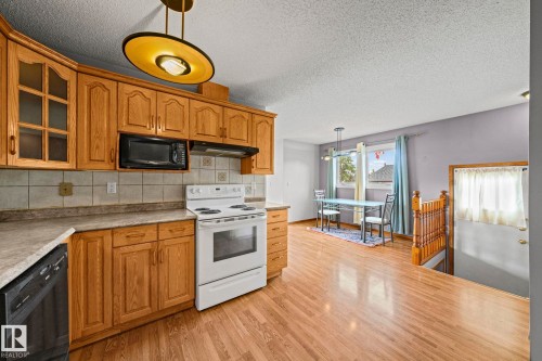 Kitchen featuring wood cabinetry, solid surface countertops, tile backsplash, and wood-finish flooring - 17908 92A Street Nw, Edmonton, AB - Indoor Photo Showing Kitchen