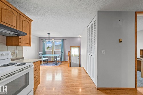 Light wood-finish flooring throughout, white range, wood cabinetry, and a dining area with a contemporary chandelier - 17908 92A Street Nw, Edmonton, AB - Indoor Photo Showing Kitchen