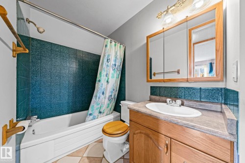 Bathroom featuring a white bathtub, tiled shower surround, wood-finish vanity with an integrated sink, and a mirrored medicine cabinet - 17908 92A Street Nw, Edmonton, AB - Indoor Photo Showing Bathroom