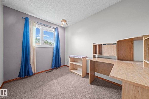 Carpeted room featuring a single window, built-in shelving, and a built-in desk with overhead storage - 17908 92A Street Nw, Edmonton, AB - Indoor