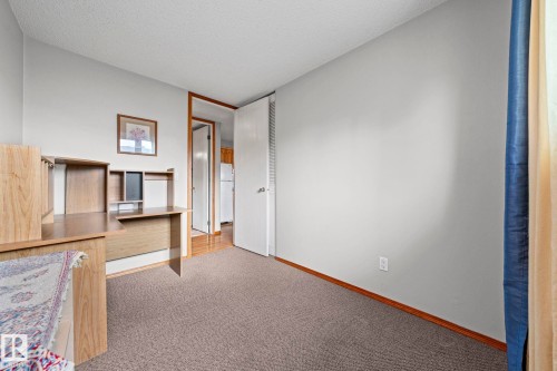 Wall-to-wall carpeting with light-toned walls, featuring a built-in wood-finish desk unit and overhead shelving - 17908 92A Street Nw, Edmonton, AB - Indoor Photo Showing Other Room
