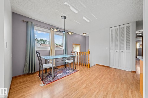 Wood-finish flooring, white louvered bifold doors, window with light-filtering curtains, overhead light fixture, and wood railing with balusters - 17908 92A Street Nw, Edmonton, AB - Indoor