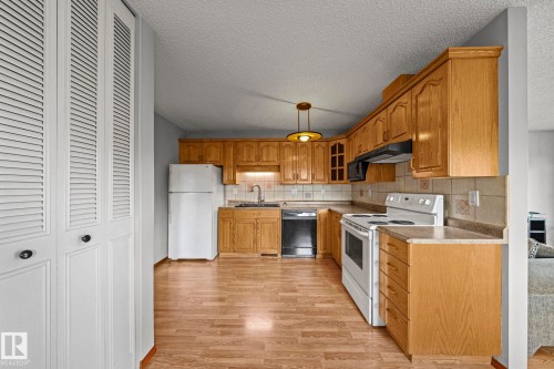 Wood-finish flooring, white louvered bifold doors, light-toned wood cabinetry, built-in microwave, and a white range - 17908 92A Street Nw, Edmonton, AB - Indoor Photo Showing Kitchen
