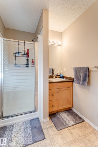 Shower enclosure with clear and frosted glass, light wood-finish vanity with countertop, wall-mounted mirror, and vanity lighting - 6218 1A Avenue Sw, Edmonton, AB - Indoor Photo Showing Bathroom