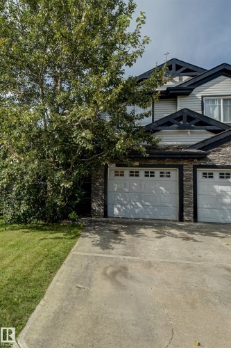 Exterior featuring white siding, dark trim accents, stone-look lower facade, and white garage doors - 6218 1A Avenue Sw, Edmonton, AB - Outdoor