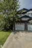 Exterior featuring white siding, dark trim accents, stone-look lower facade, and white garage doors - 6218 1A Avenue Sw, Edmonton, AB  - Outdoor 