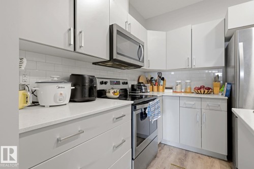 White shaker-style cabinetry, stainless steel appliances, light-toned countertops, and subway tile backsplash - #147 1818 Rutherford Rd Sw, Edmonton, AB - Indoor Photo Showing Kitchen
