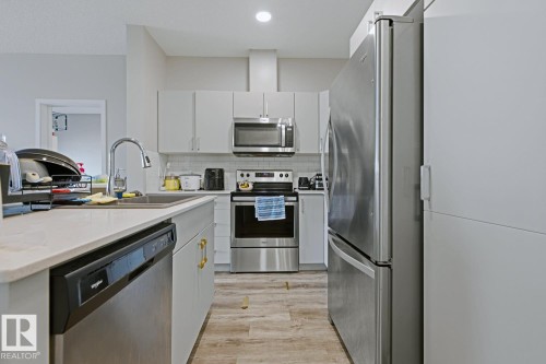 Contemporary kitchen featuring light gray cabinetry, stainless steel appliances, a white subway tile backsplash, and a light-toned wood-finish flooring - #147 1818 Rutherford Rd Sw, Edmonton, AB - Indoor Photo Showing Kitchen With Upgraded Kitchen