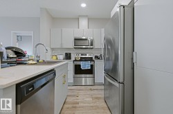 Contemporary kitchen featuring light gray cabinetry, stainless steel appliances, a white subway tile backsplash, and a light-toned wood-finish flooring - 