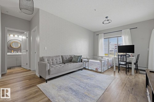Wood-finish flooring throughout, light-colored walls, and a window with horizontal blinds - #147 1818 Rutherford Rd Sw, Edmonton, AB - Indoor Photo Showing Living Room