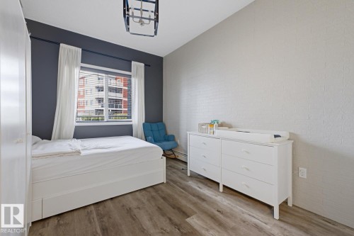 Recessed window with blinds and white curtains, wood-finish flooring, and a ceiling-mounted light fixture - #147 1818 Rutherford Rd Sw, Edmonton, AB - Indoor Photo Showing Bedroom