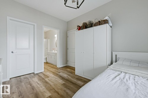 Wood-finish flooring throughout, white interior doors with satin nickel hardware, and an overhead light fixture - #147 1818 Rutherford Rd Sw, Edmonton, AB - Indoor Photo Showing Bedroom
