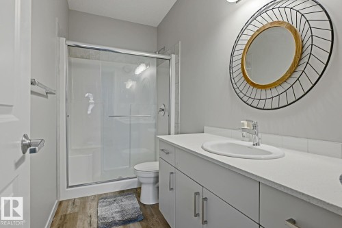 Wood-finish flooring, white vanity with integrated sink, chrome faucet, and glass-enclosed shower with sliding door - #147 1818 Rutherford Rd Sw, Edmonton, AB - Indoor Photo Showing Bathroom