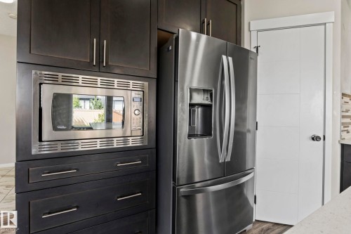 Stainless steel French door refrigerator, built-in stainless steel microwave, dark wood-finish cabinetry, and white paneled door - 5210 23 Ave Sw, Edmonton, AB - Indoor Photo Showing Kitchen