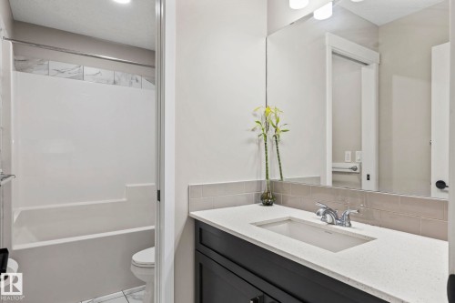 Built-in bathtub with a tile surround, dark wood-finish vanity, white countertop, and a large wall-mounted mirror - 5210 23 Ave Sw, Edmonton, AB - Indoor Photo Showing Bathroom