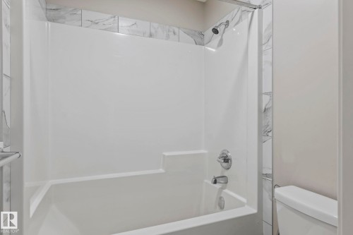 White bathtub and shower combination with chrome fixtures and marble-look tile accents - 5210 23 Ave Sw, Edmonton, AB - Indoor Photo Showing Bathroom