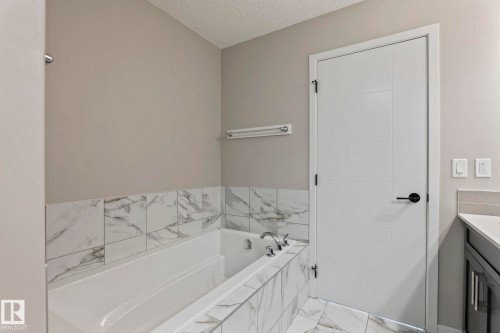 Soaking tub with tile surround, modern white door, and grey wall color - 5210 23 Ave Sw, Edmonton, AB - Indoor Photo Showing Bathroom