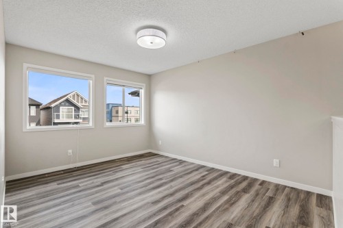 Wood-finish flooring, two windows with white trim, neutral wall color, and a ceiling-mounted light fixture - 5210 23 Ave Sw, Edmonton, AB - Indoor Photo Showing Other Room