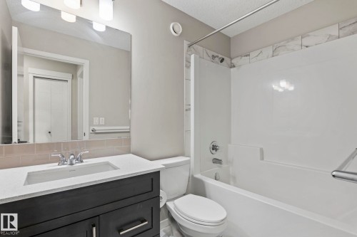 Bathroom with a dark wood-finish vanity, integrated rectangular sink, light-toned countertop, and a full-size mirror - 5210 23 Ave Sw, Edmonton, AB - Indoor Photo Showing Bathroom