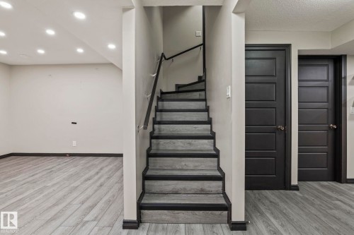 Wood-finish flooring, recessed lighting, modern dark panel doors, and a staircase with a dark handrail - 5210 23 Ave Sw, Edmonton, AB - Indoor Photo Showing Other Room