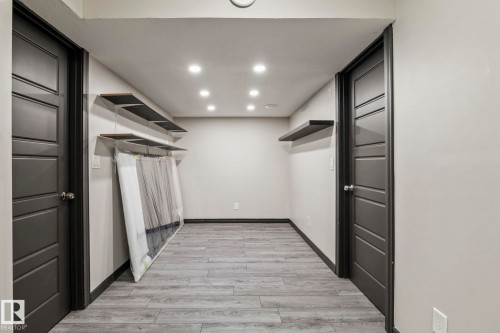 Recessed lighting illuminating wood-finish flooring, two dark paneled doors, and two wall-mounted shelves - 5210 23 Ave Sw, Edmonton, AB - Indoor