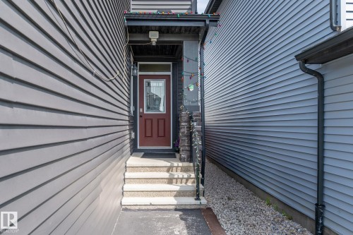 Red entry door with an upper glass panel, stone-accented railing, covered entryway, and light-colored siding - 5210 23 Ave Sw, Edmonton, AB - Outdoor