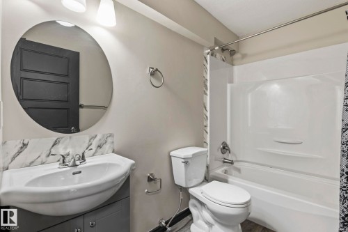 Vanity with integrated sink, modern circular mirror, two-light fixture, white bathtub, and toilet - 5210 23 Ave Sw, Edmonton, AB - Indoor Photo Showing Bathroom