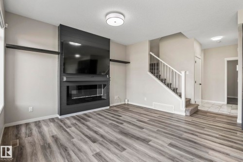Wood-finish flooring, built-in fireplace, staircase with metal balusters, ceiling-mounted lighting, and neutral wall tones - 5210 23 Ave Sw, Edmonton, AB - Indoor Photo Showing Living Room With Fireplace