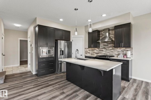 Kitchen featuring dark cabinetry, stainless steel appliances, a center island with a light-toned countertop, and wood-finish flooring - 5210 23 Ave Sw, Edmonton, AB - Indoor Photo Showing Kitchen With Upgraded Kitchen