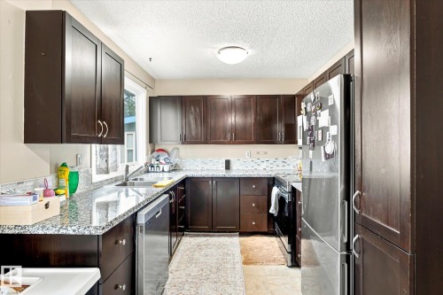 U-shaped kitchen with dark wood-finish cabinetry, light speckled countertops, and a full-height tile backsplash - 6471 180 Street Nw, Edmonton, AB - Indoor Photo Showing Kitchen With Double Sink