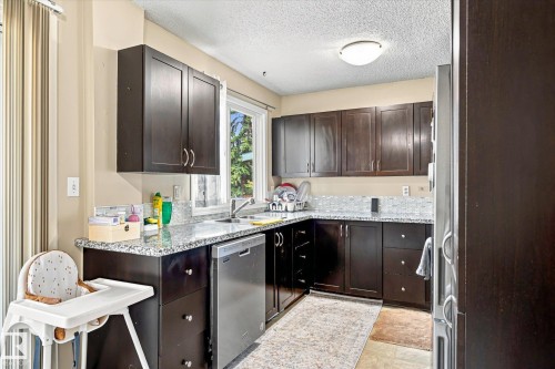 U-shaped kitchen with dark wood-finish cabinetry, light-colored granite countertops, and a mosaic tile backsplash - 6471 180 Street Nw, Edmonton, AB - Indoor Photo Showing Kitchen