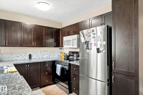 Dark wood-finish cabinetry, stainless steel appliances, granite-style countertops, and a mosaic tile backsplash - 6471 180 Street Nw, Edmonton, AB - Indoor Photo Showing Kitchen With Stainless Steel Kitchen