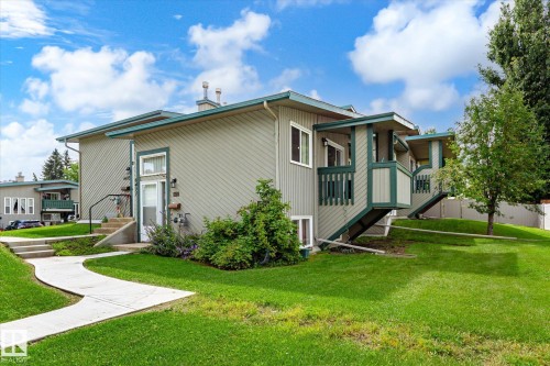 Light gray siding exterior with dark green trim, multiple private balconies, concrete walkways, and green landscaping - 6471 180 Street Nw, Edmonton, AB - Outdoor