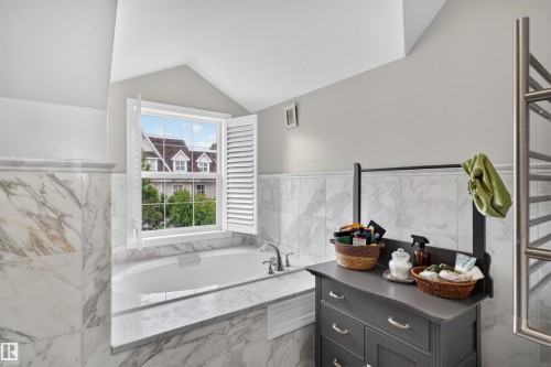 Built-in soaking tub, white plantation shutters, white window frame, marble-finish tile surround, and a wall-mounted towel warmer - 4471 Mccrae Avenue Nw, Edmonton, AB - Indoor Photo Showing Bathroom