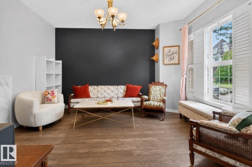 Wood-finish flooring, plantation shutters, built-in shelving, and a wall-mounted chandelier - 4471 Mccrae Avenue Nw, Edmonton, AB - Indoor Photo Showing Living Room