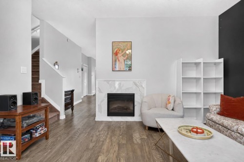 Wood-finish flooring throughout, a modern electric fireplace with a marble-look surround, and a built-in shelving unit - 4471 Mccrae Avenue Nw, Edmonton, AB - Indoor Photo Showing Living Room With Fireplace
