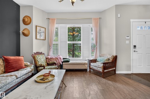 Wood-finish flooring, bay window with plantation shutters, white paneled entry door with decorative glass inserts, and a decorative light fixture - 4471 Mccrae Avenue Nw, Edmonton, AB - Indoor Photo Showing Living Room