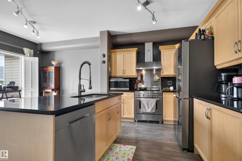 Kitchen featuring light wood cabinetry, dark countertops, wood-finish flooring, stainless steel appliances, and track lighting - 4471 Mccrae Avenue Nw, Edmonton, AB - Indoor Photo Showing Kitchen With Double Sink